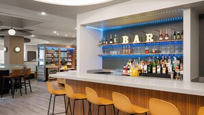 Un espace bar doté d’un comptoir blanc, de plusieurs étagères remplies de bouteilles et de tabourets de bar jaunes.
