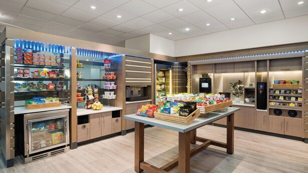 Un espace de vente moderne, doté d’étagères remplies d’en-cas, d’un présentoir réfrigéré et d’une table centrale où sont exposés des produits emballés.