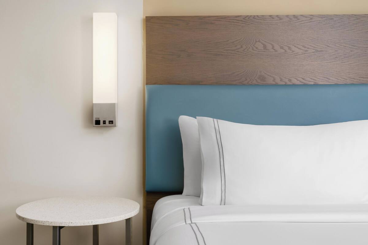 A hotel room with a bed, a round table, and a wall-mounted light fixture.
