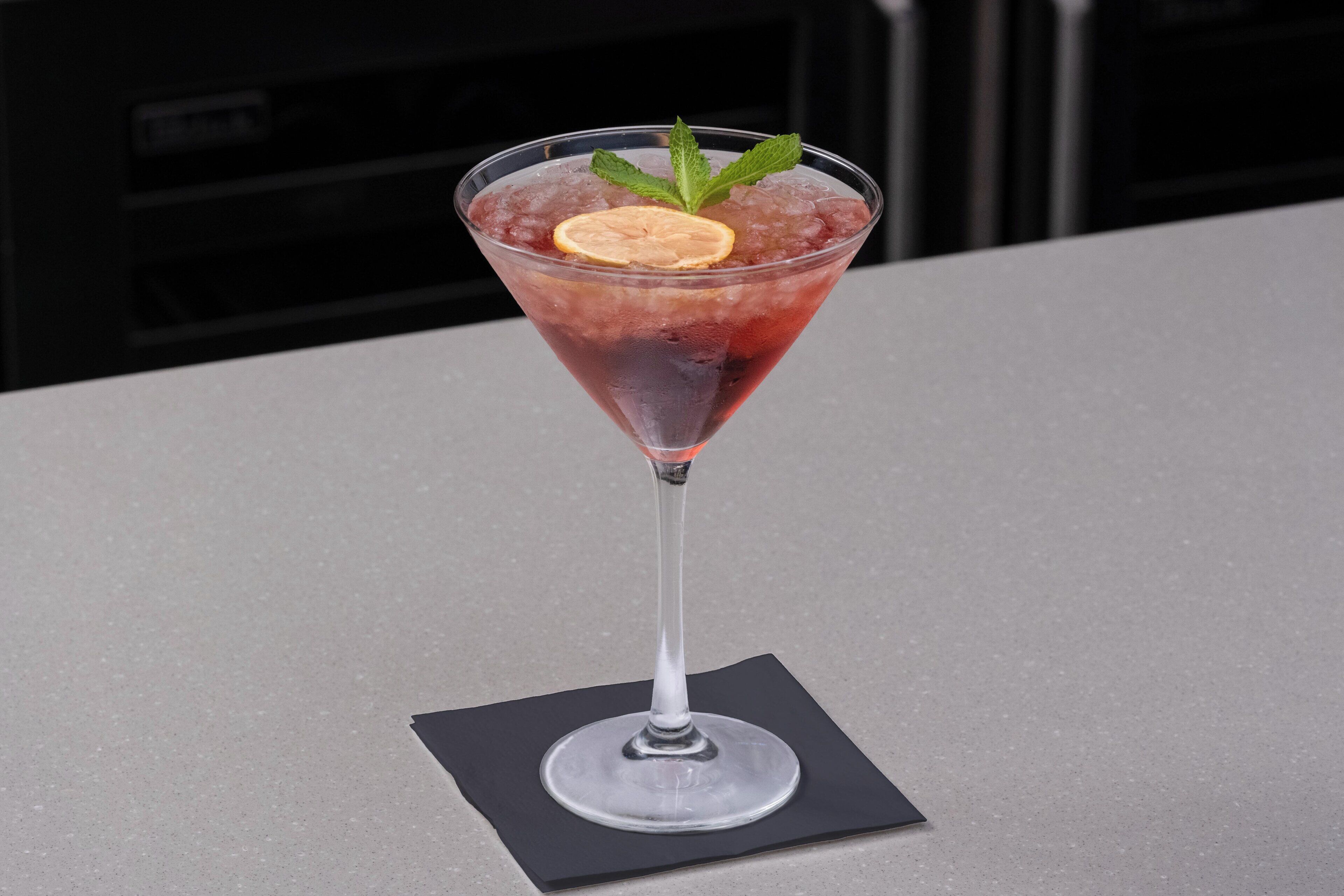 A martini glass with a lemon slice and mint garnish on a table.