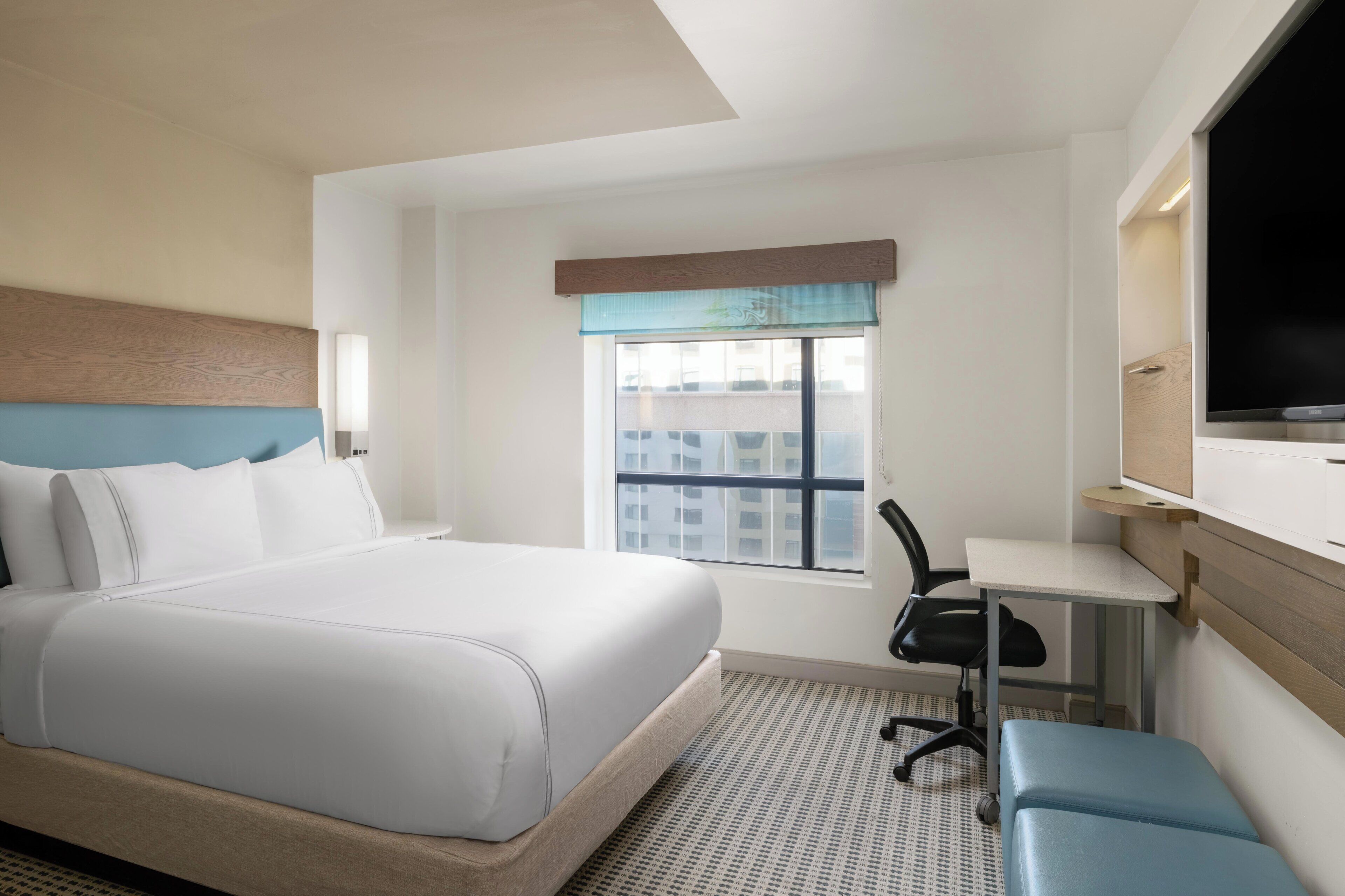 A hotel room with a bed, desk, chair, TV, and window.