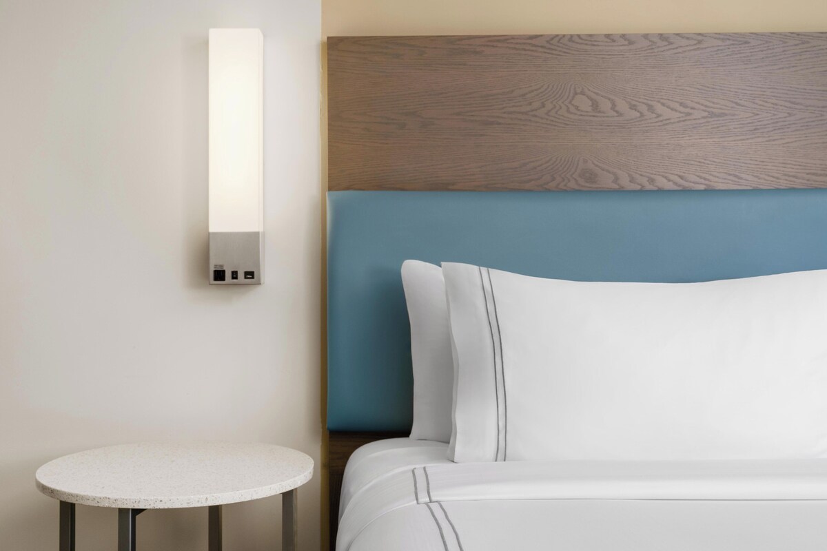 Una habitación de hotel con una cama, una mesa redonda y una lámpara fijada a la pared.