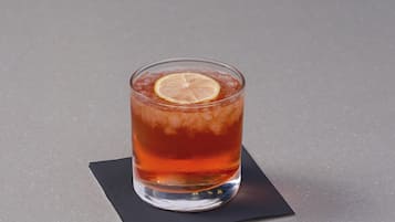 Un vaso de té helado con una rodaja de limón sobre un posavasos oscuro.