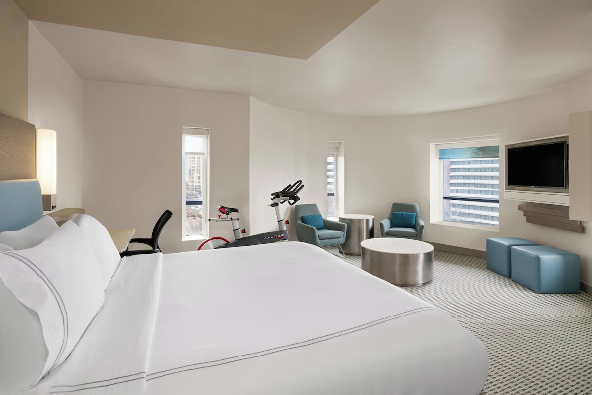 A hotel room with a large bed, a desk, two chairs, a small table, a TV, and a bike.