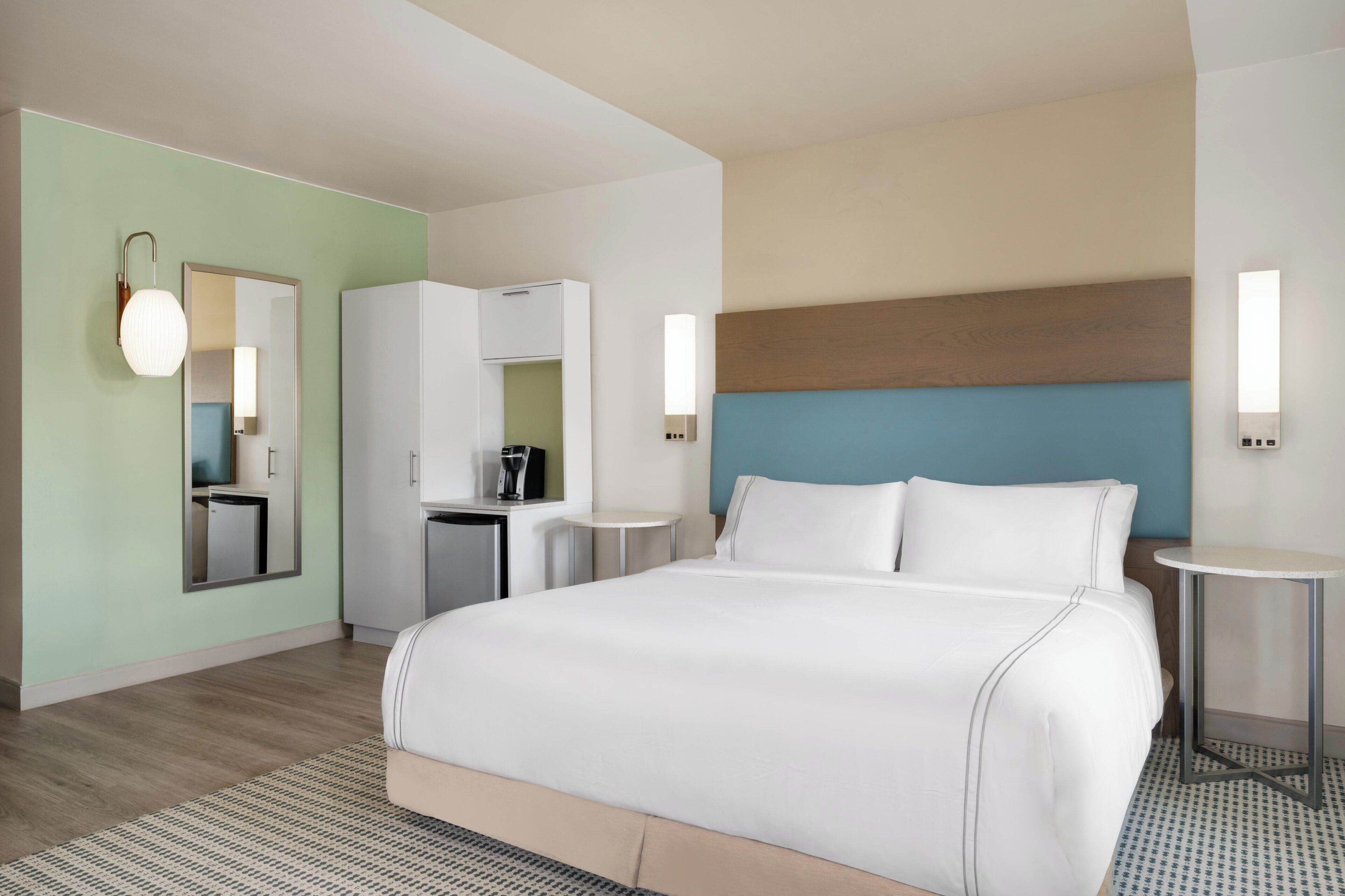 A hotel room with a bed, a small kitchenette, a mirror, and a round table.