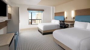 Une chambre d’hôtel avec deux lits, un bureau, une chaise, une télévision et une fenêtre donnant sur la ville.