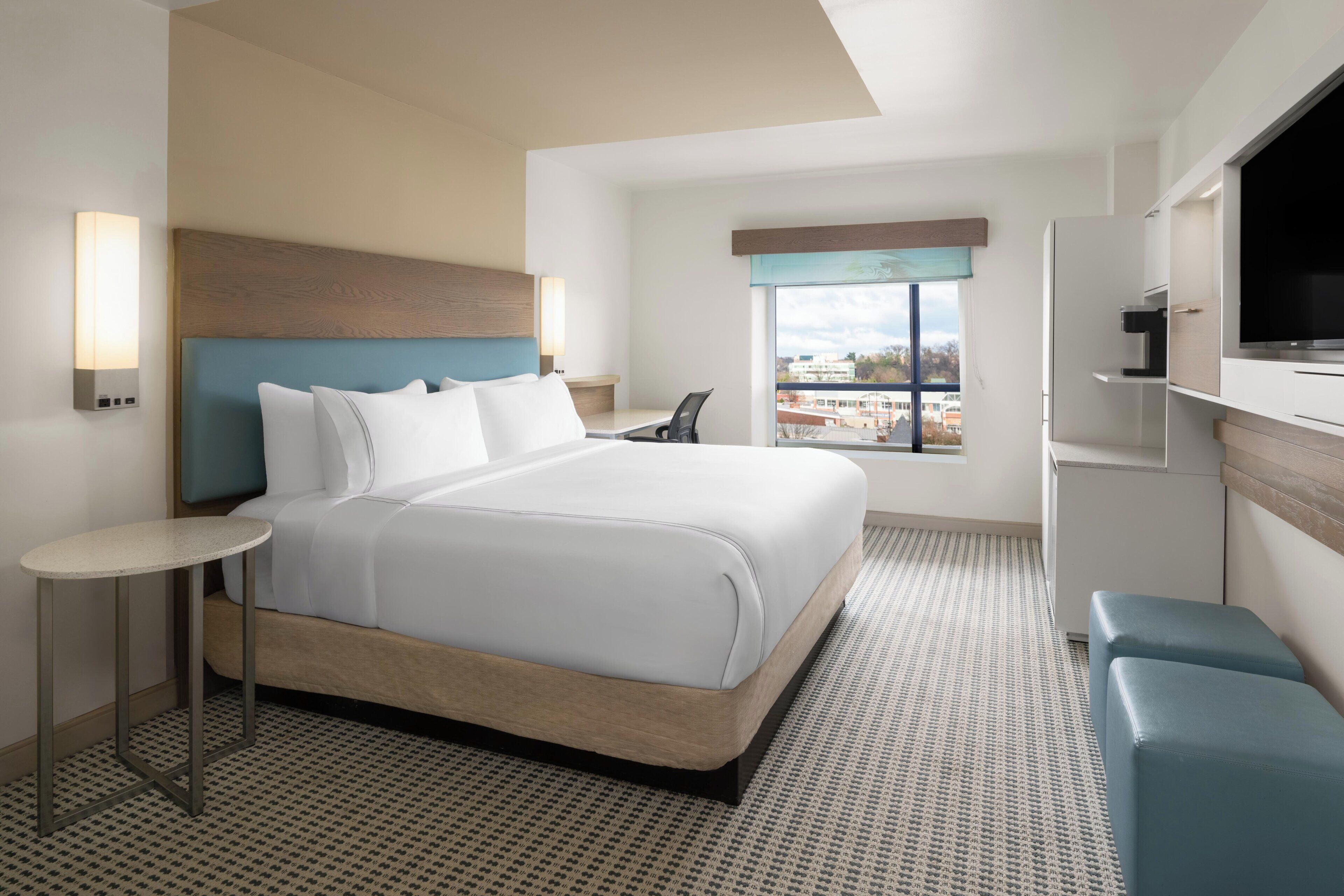 Een moderne hotelkamer met een groot bed, een klein tafeltje, een televisie en een raam met uitzicht op de stad.