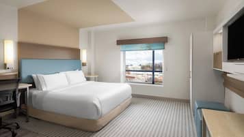 A hotel room with a bed, a desk, a chair, a TV, and a window with a view.