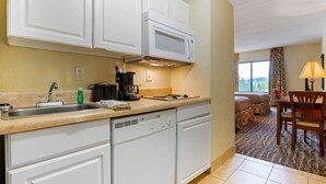 A kitchen with white cabinets, a microwave, and a coffee maker. There is a sink with a faucet and a countertop with various items.