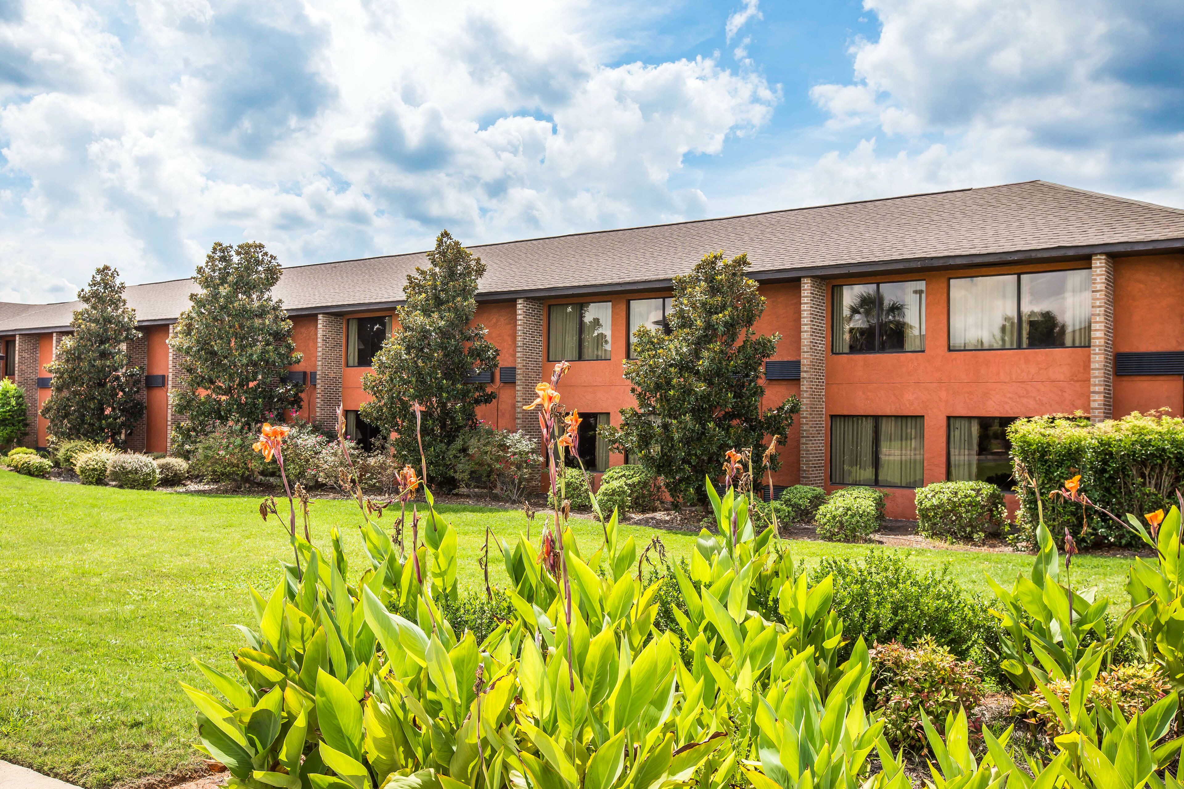 A multi-story building with a brick facade, large windows, and a well-maintained lawn with various plants.