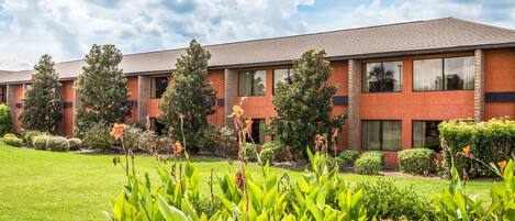 A multi-story building with a brick facade, large windows, and a well-maintained lawn with various plants.