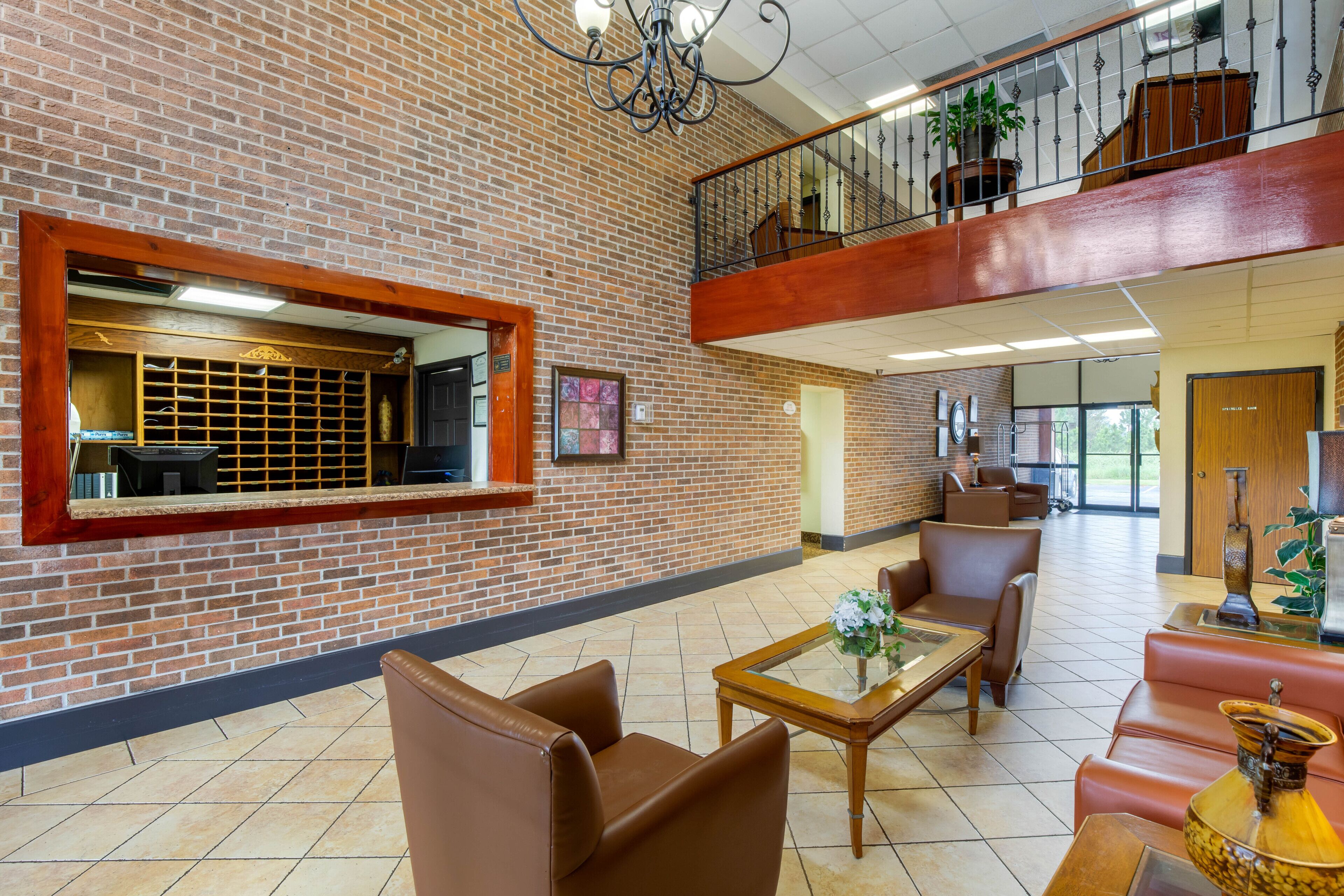 A lobby with a brick wall, a wooden reception desk, seating areas, and a staircase to an upper level.