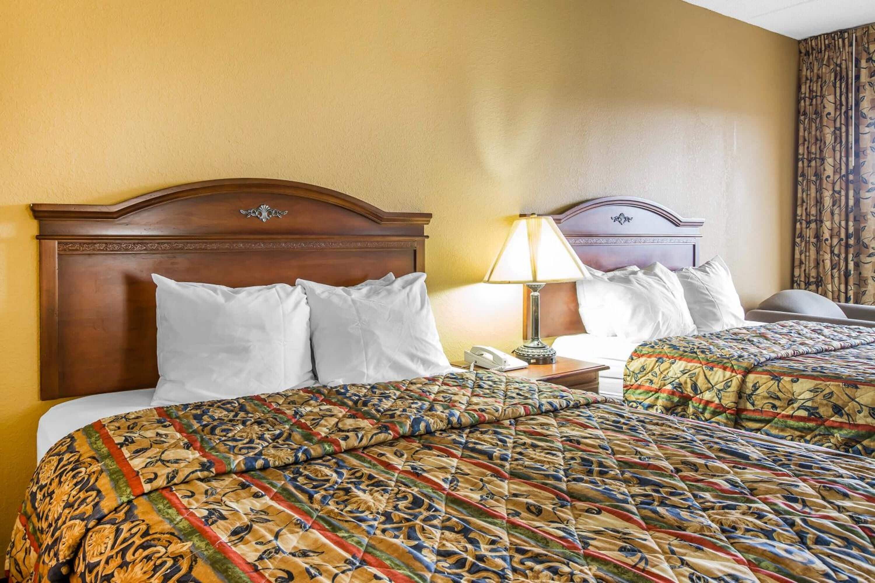 A hotel room with two beds, a wooden headboard, a bedside table with a lamp, and a telephone.