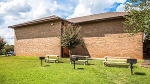 A brick building with a flat roof, two benches, and a mailbox in a grassy area.