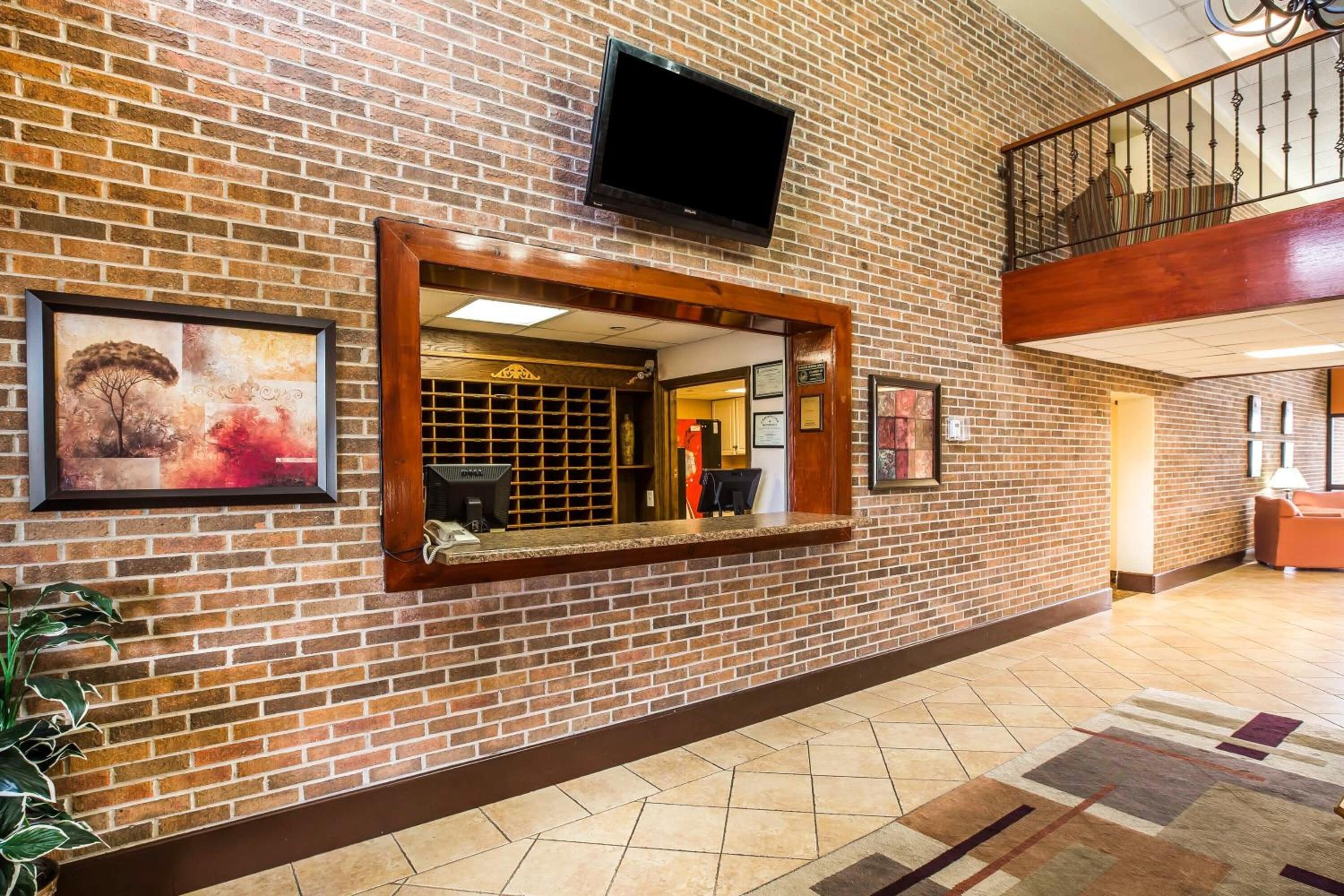 A lobby with a brick wall, a reception desk, a television mounted above it, and a staircase to the upper level.
