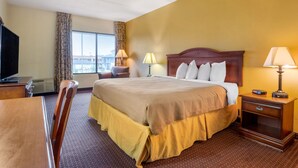 A hotel room with a large bed, a desk, a chair, a TV, and a window with curtains.