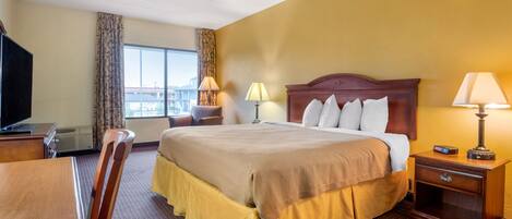 A hotel room with a large bed, a desk, a chair, a TV, and a window with curtains.