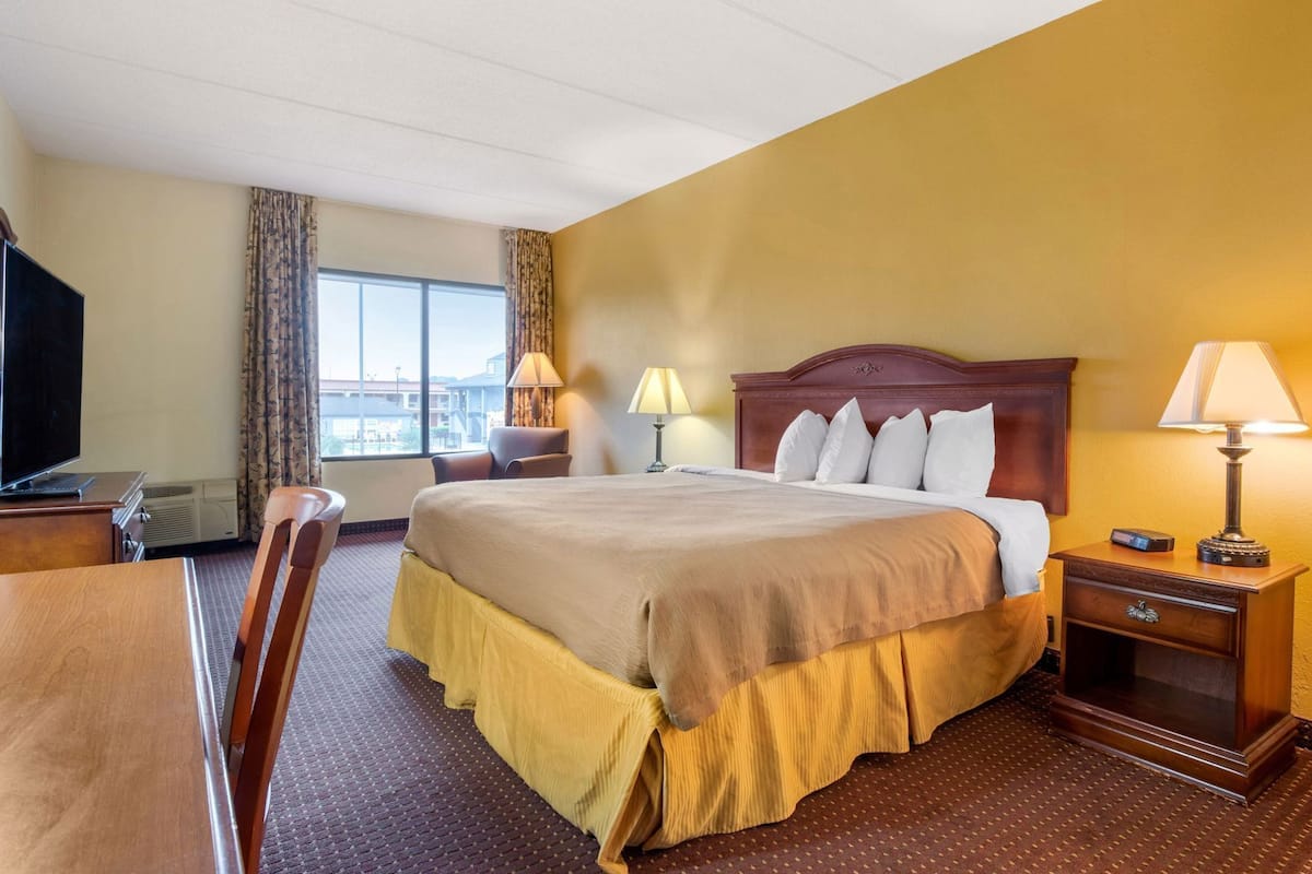 A hotel room with a bed, a desk, a chair, a TV, and a window.