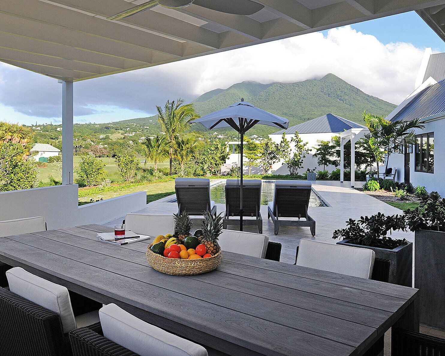An outdoor seating area with a wooden table, chairs, and a fruit basket.
