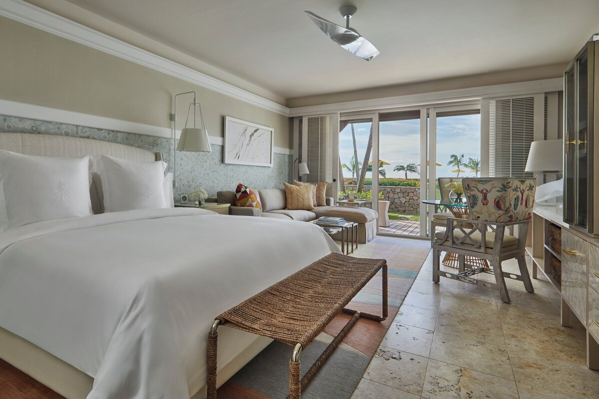 A hotel room with a large bed, a small sofa, a dining table, and a view of the outdoors.