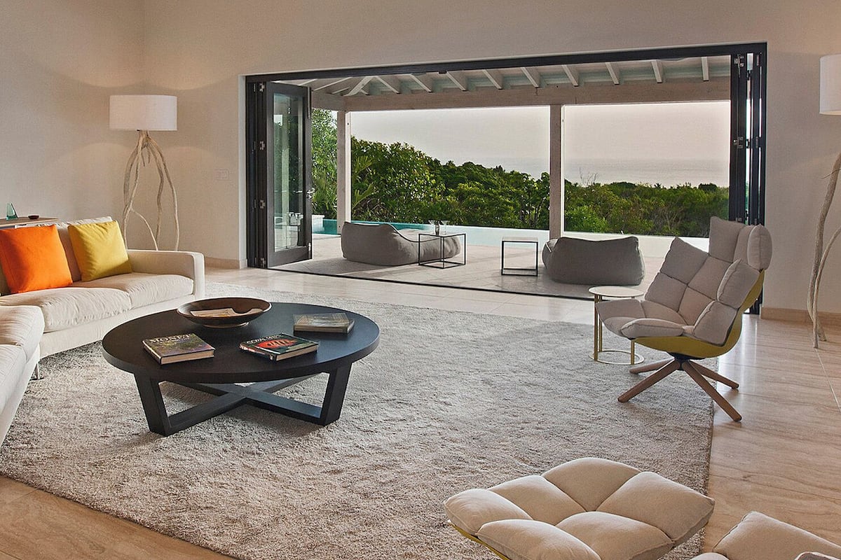 A modern living room with a sofa, a coffee table, and a chair. There is a large glass door leading to an outdoor area.