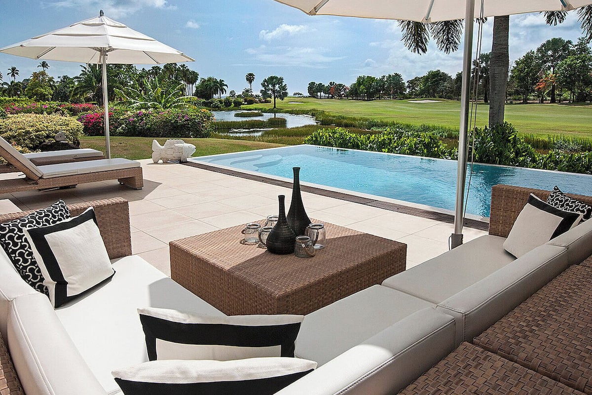 A poolside area with a white sofa, two white umbrellas, and a wicker coffee table.