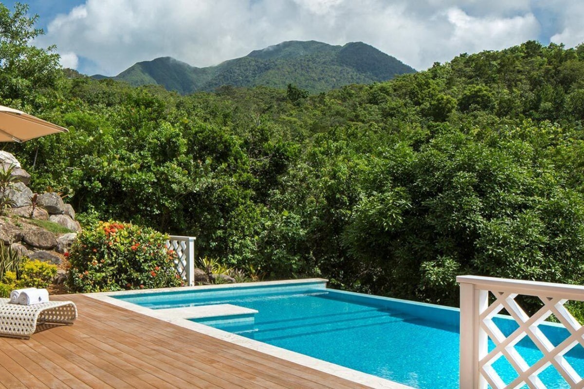 A wooden deck with lounge chairs and an umbrella, overlooking a swimming pool and lush greenery.
