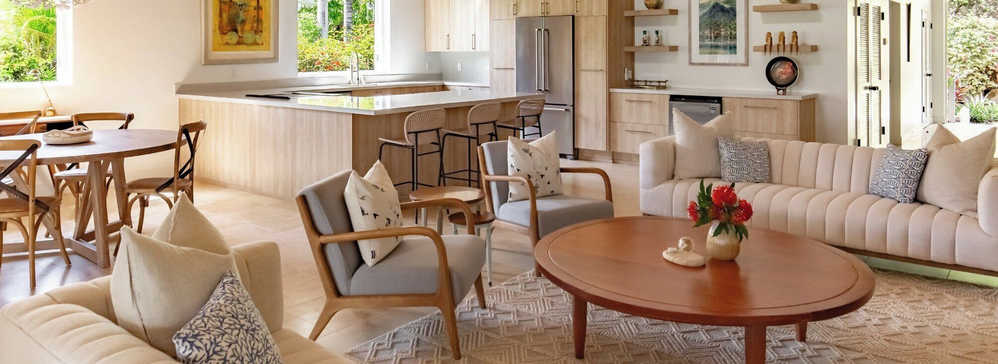 A modern living room with a sofa, chairs, a coffee table, and a kitchen area with a refrigerator and bar stools.