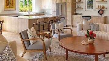 A modern living room with a sofa, chairs, a coffee table, and a kitchen area with a refrigerator and bar stools.