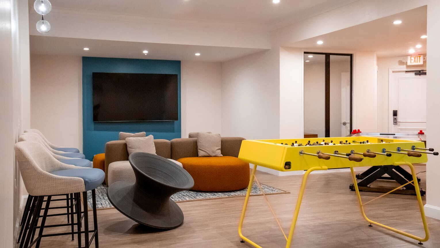 Una sala de estar moderna con una mesa de fútbol de mesa, un televisor de pantalla plana grande y un sofá con cojines.