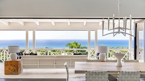 A modern outdoor seating area with a view of the ocean, white furniture, and a chandelier. - Four Seasons Resort - Nevis (Jessups Village)