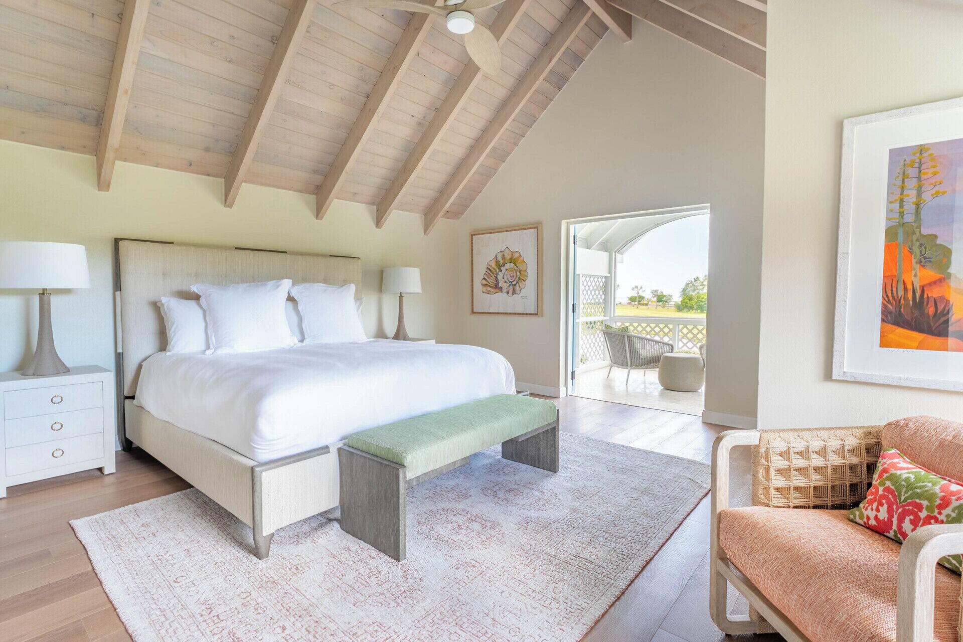 A spacious bedroom with a large bed, a bench, a chair, and a view to an outdoor area.