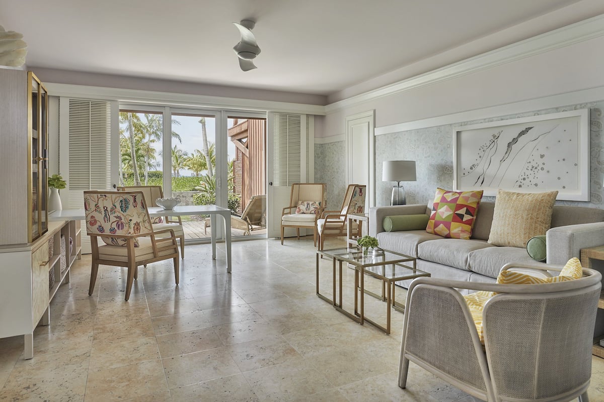 A spacious living room with a large window, a sofa, a coffee table, and two chairs.