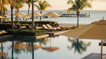 A poolside area with lounge chairs and umbrellas, a wooden deck, and a view of the ocean.
