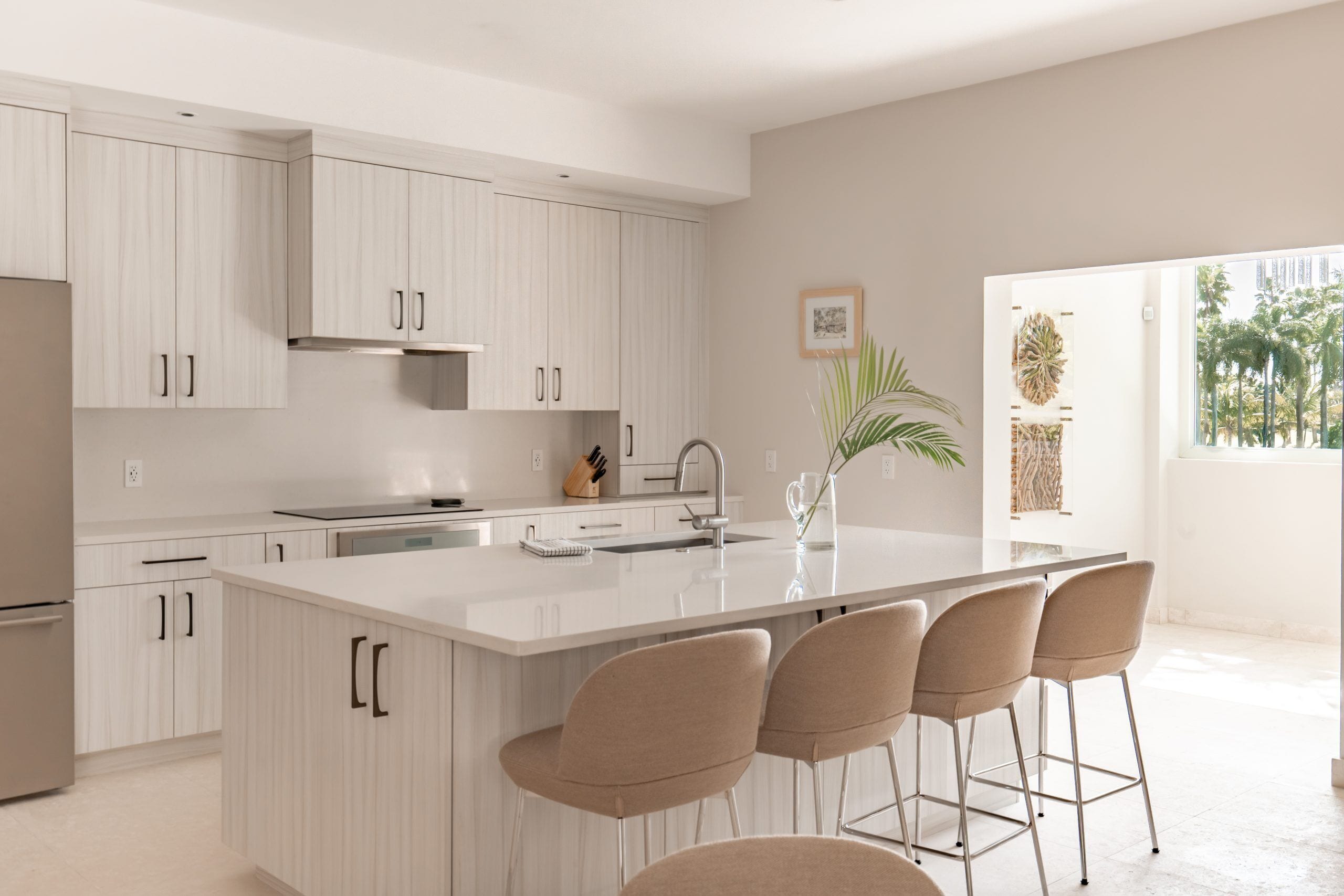 A modern kitchen with white cabinetry, a central island with bar stools, and a large window providing natural light.