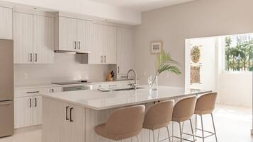 A modern kitchen with white cabinetry, a central island with bar stools, and a large window providing natural light.