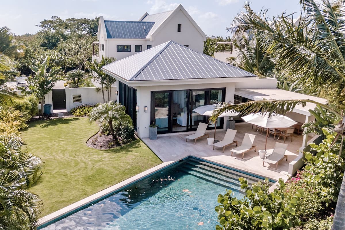 A modern house with a swimming pool, surrounded by lush greenery and palm trees.