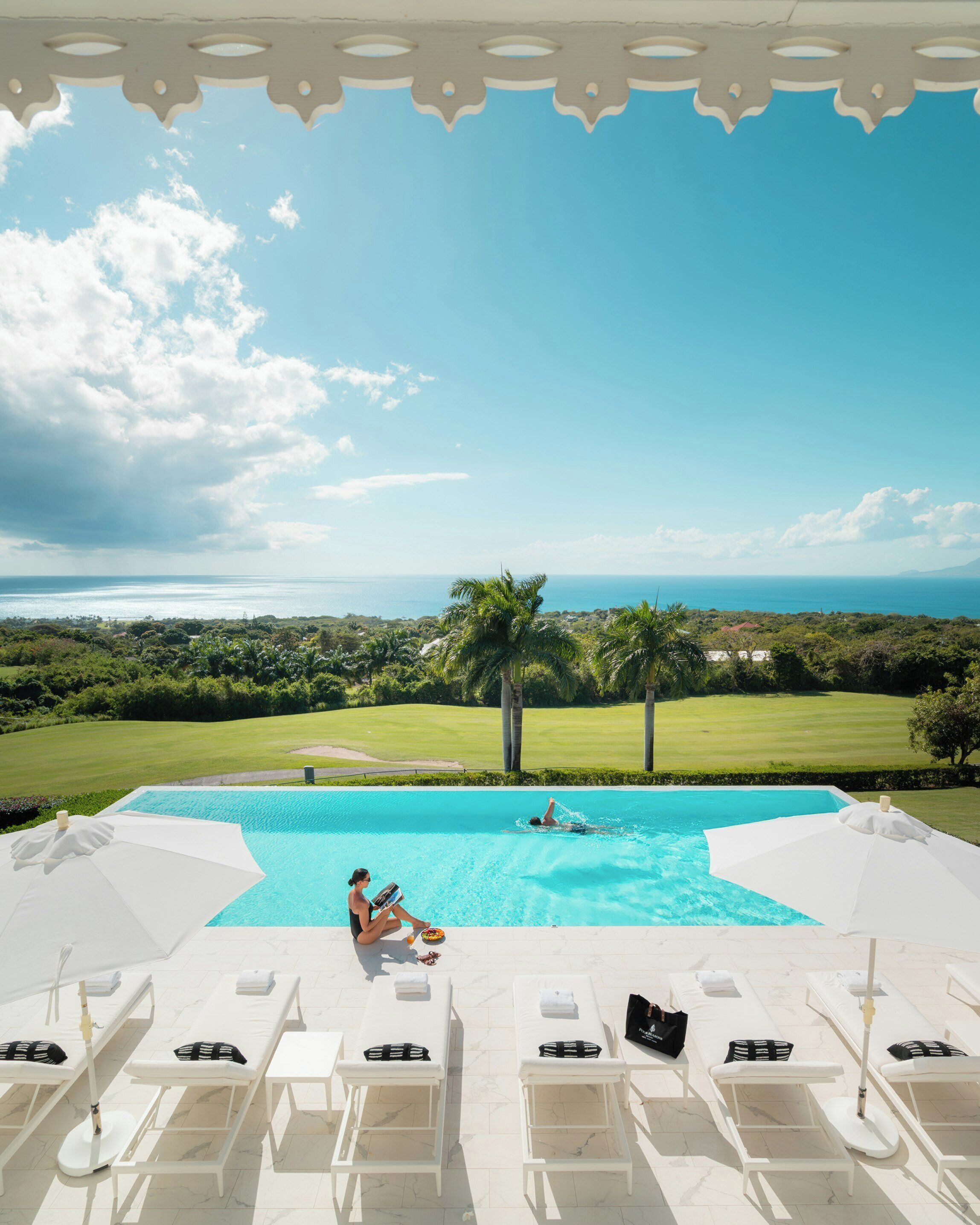 A poolside area with lounge chairs, a swimming pool, and a view of the ocean and greenery.