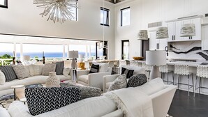 A spacious living area with a large sofa set, a dining area with bar stools, and a kitchen with white cabinets and pendant lighting. - Four Seasons Resort - Nevis (Jessups Village)