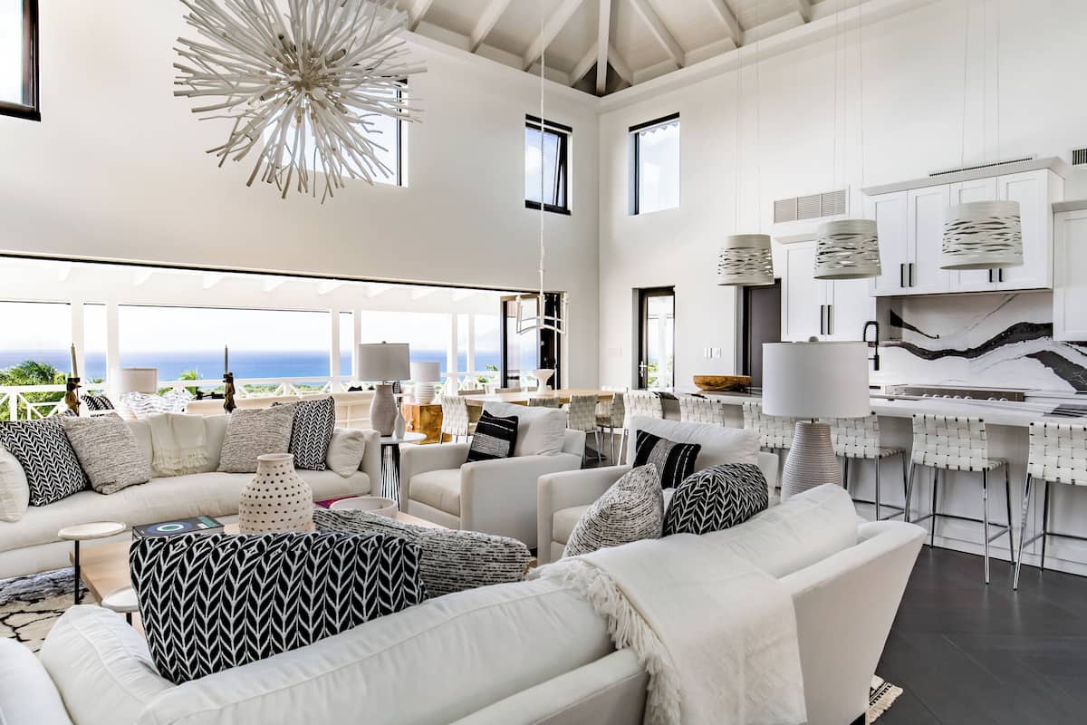A spacious living area with a large sofa set, a dining area with bar stools, and a kitchen with white cabinets and pendant lighting.