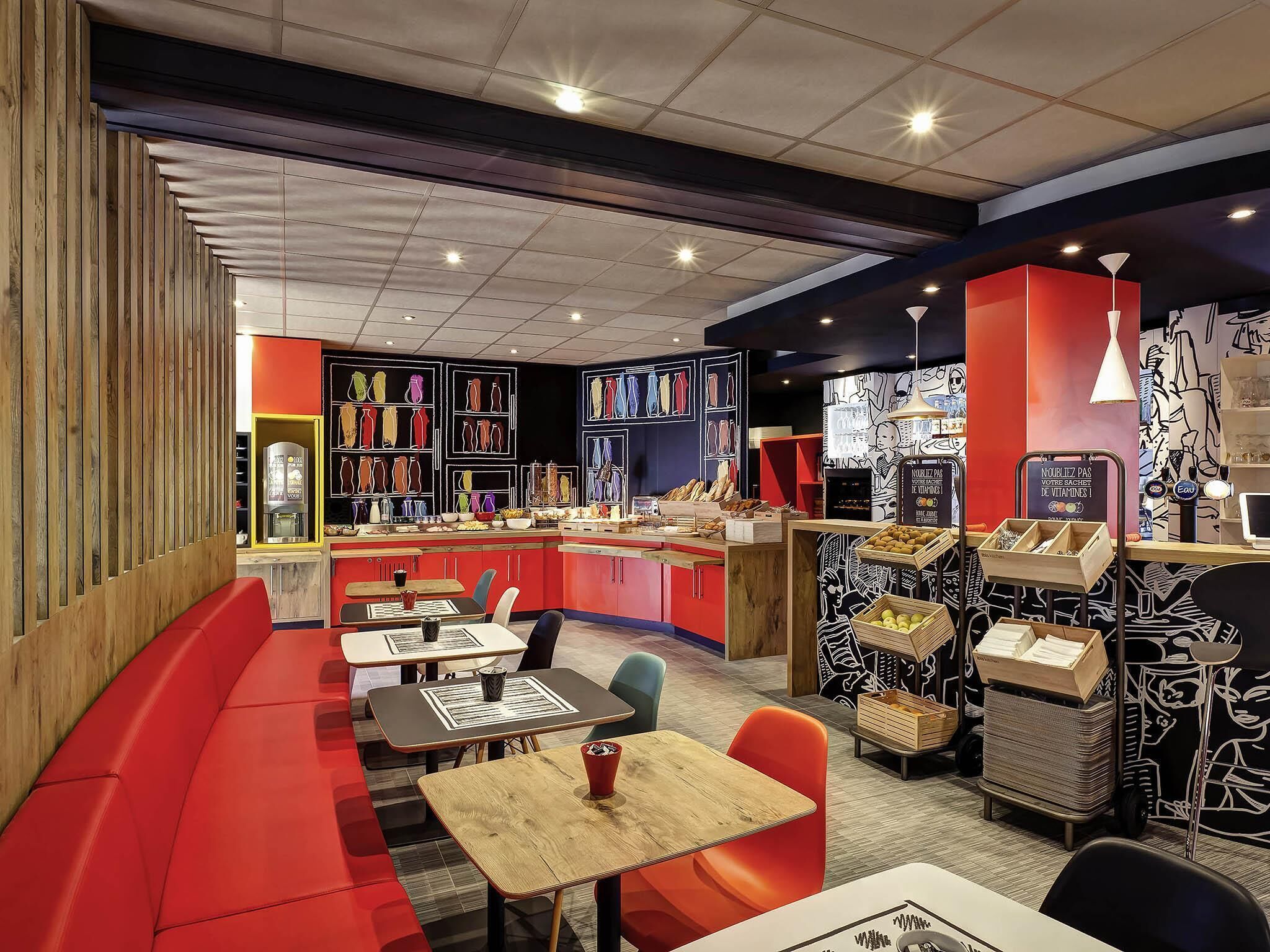 A restaurant with a red and black color scheme, featuring a counter with various food items, a seating area with tables and chairs, and a wall with framed artwork.