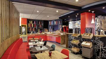 A restaurant with a red and black color scheme, featuring a counter with various food items, a seating area with tables and chairs, and a wall with framed artwork.