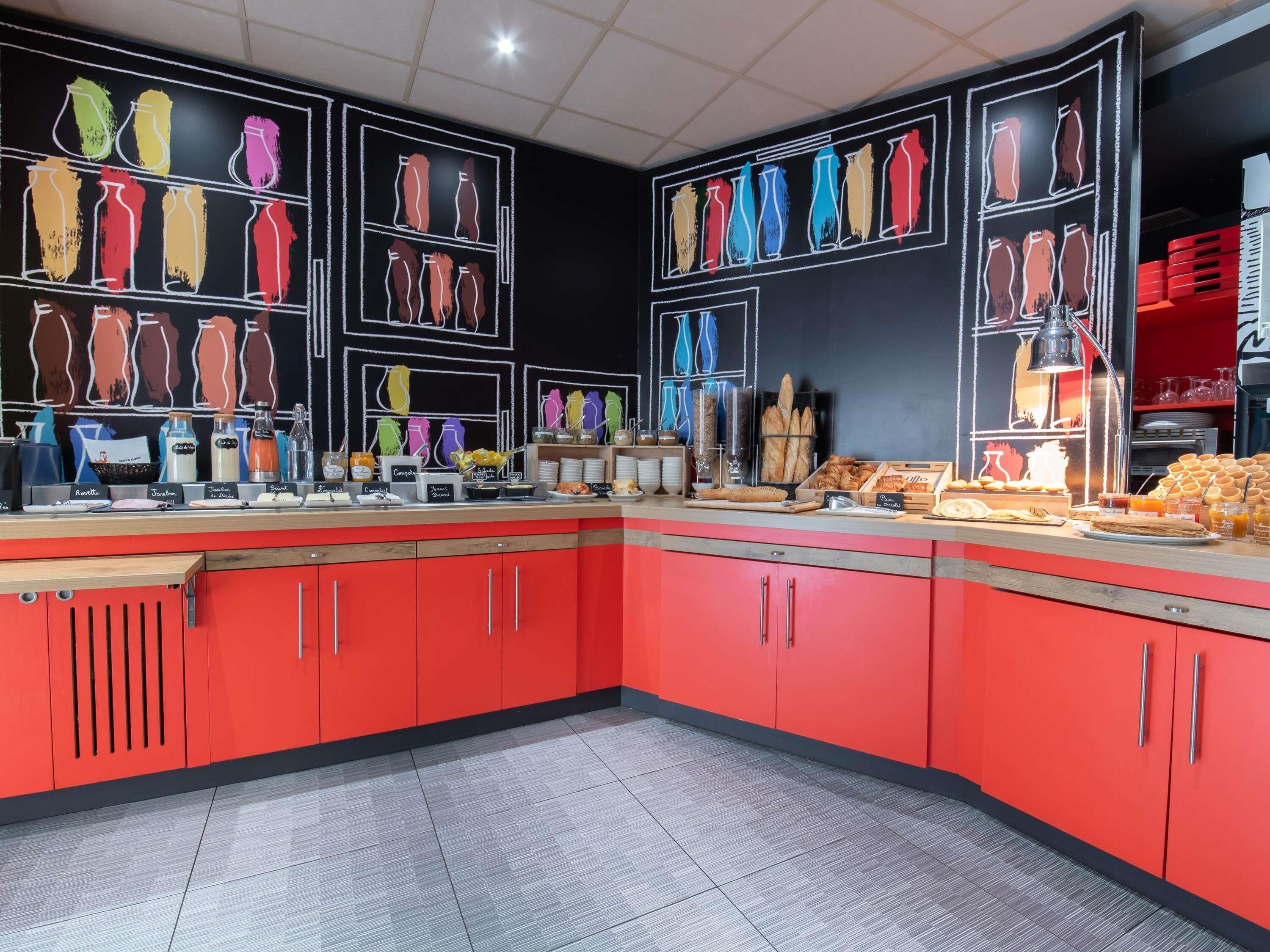 A breakfast buffet with various food items and beverages, red cabinets, and a chalkboard wall with vases.