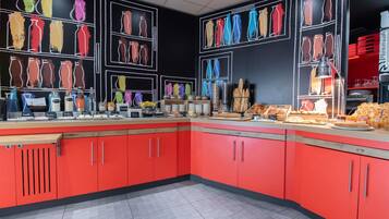 A breakfast buffet with various food items and beverages, red cabinets, and a chalkboard wall with vases.