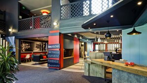 A modern interior with a bar area, a seating space, and a reception desk. - ibis Lyon Nord (Dardilly)
