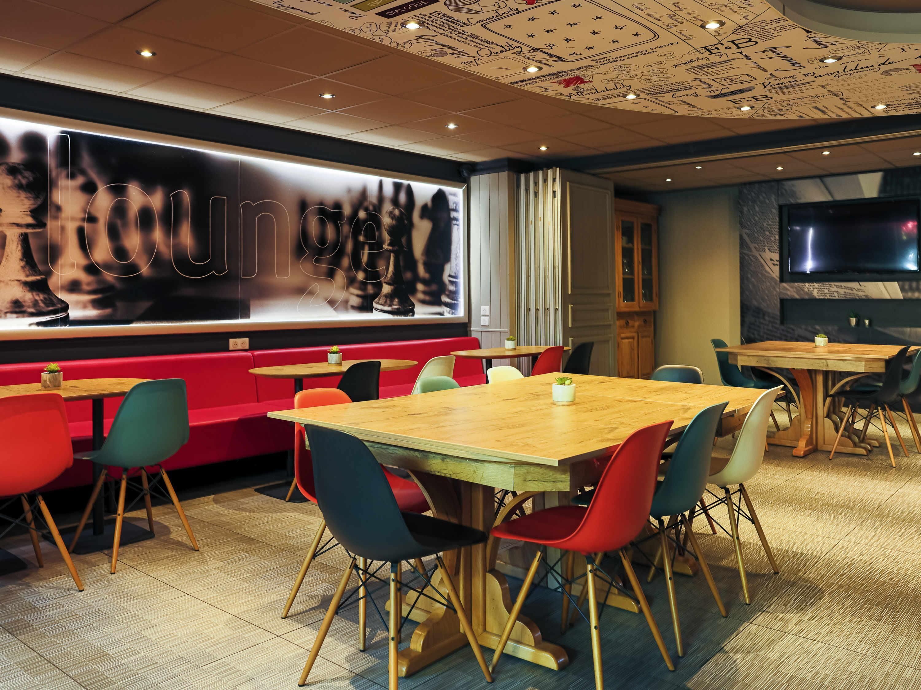 Un restaurant doté de nombreuses tables et chaises, d’une grande fresque murale et d’un téléviseur fixé au mur.