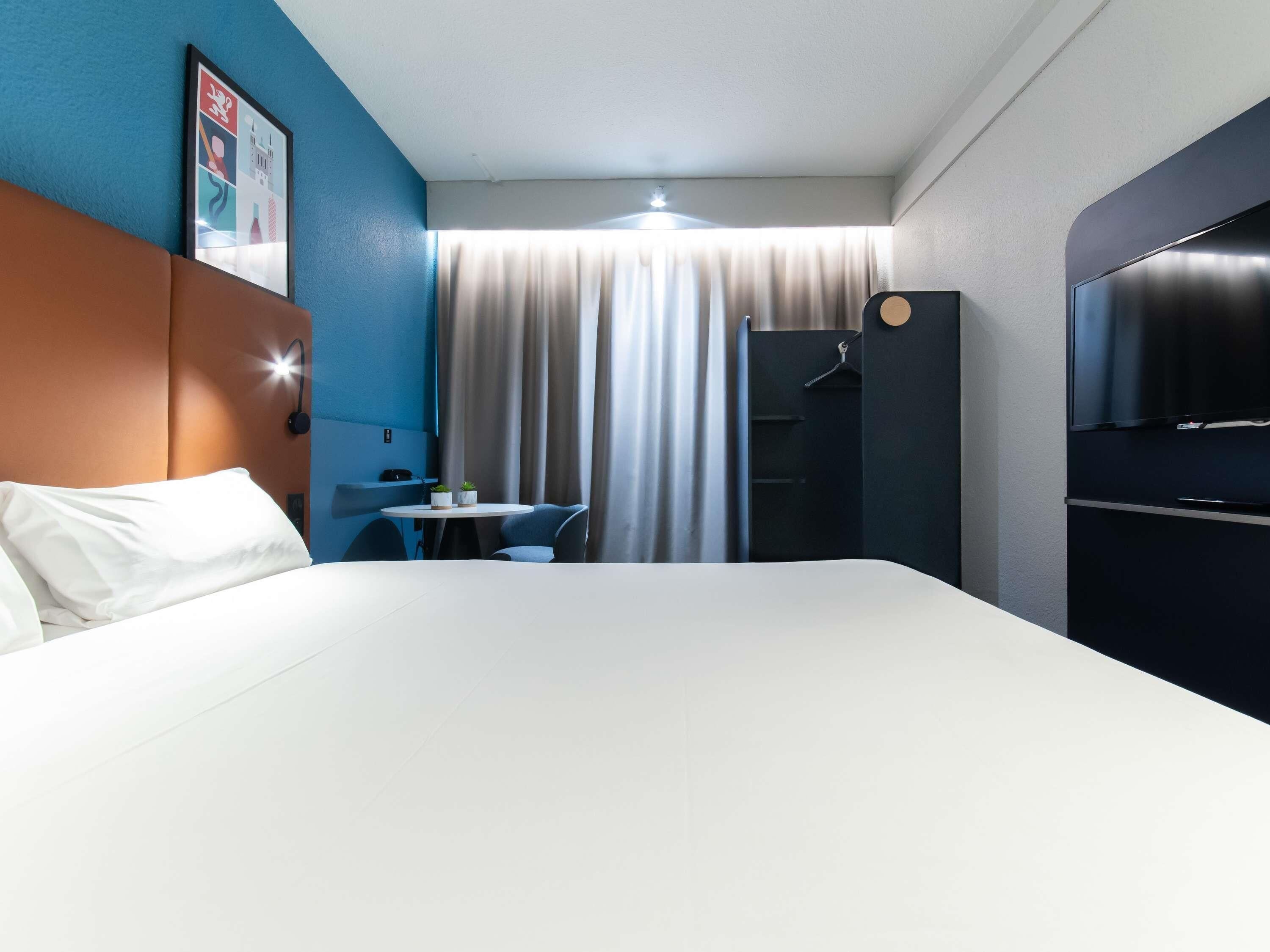 Una habitación de hotel con una cama, un escritorio, una silla, un televisor y un armario.