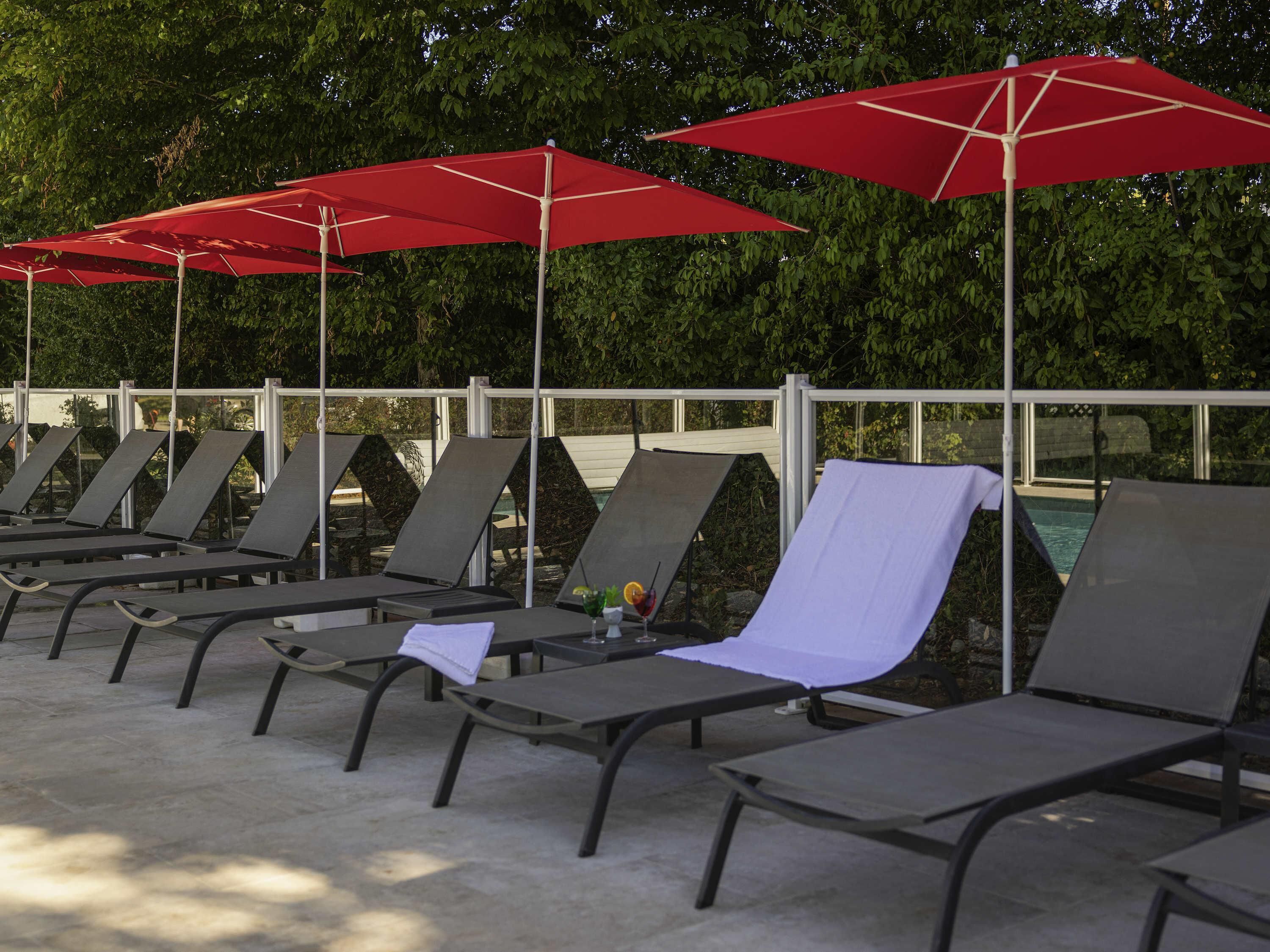 A row of lounge chairs with red umbrellas, a pool, and a metal fence.