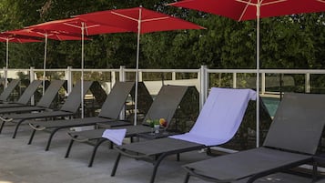 A row of lounge chairs with red umbrellas, a pool, and a metal fence.