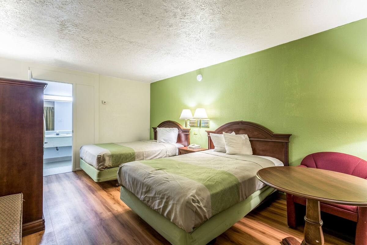 Quarto de hotel com duas camas, uma mesa de madeira e uma cadeira vermelha.
